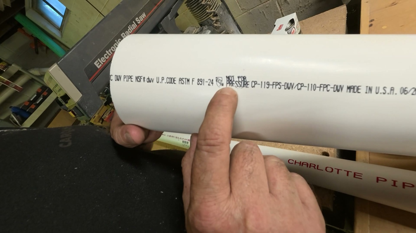 Close-up of white PVC pipe with NOT FOR PRESSURE printed on it, a finger pointing at the words